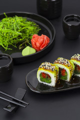 Vegetarian sushi roll with avocado ginger wasabi and chuka salad over black background