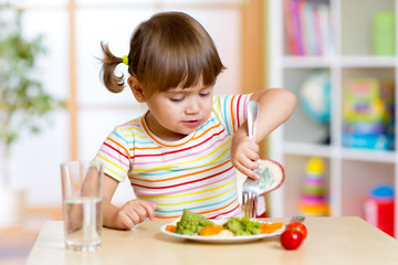 kid girl eating healthy vegetables in kindergarten or nursery