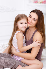 The girl and her mother sitting on a white bed in the bedroom