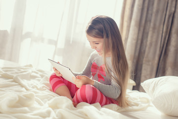 Cute little girl working with tablet computer lying in bed