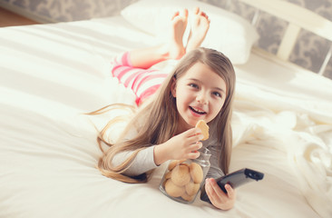 The little girl is eating oatmeal cookies in bed