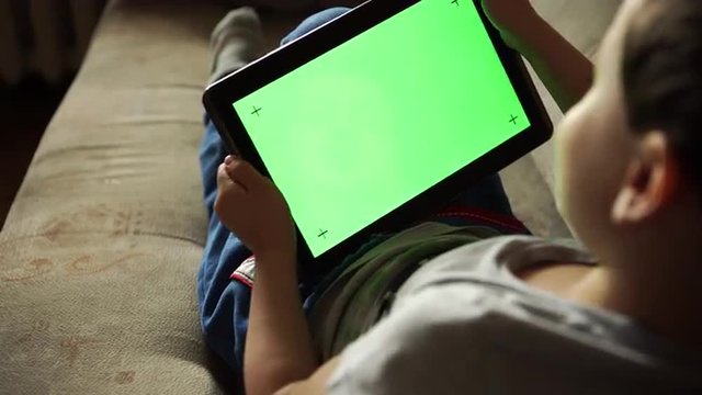 Child tilting to the left and right a tablet PC with green screen, back view