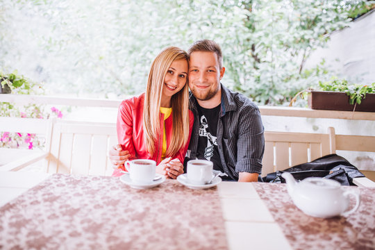beautiful young couple drink coffee hold cup, sitting on a sofa happy smile looking each other talking, portrait of lovely young man and woman on the couch