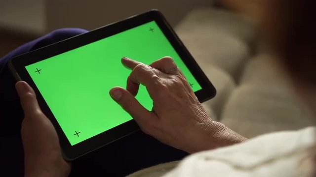 Elderly woman using a digital tablet PC with green screen, back view
