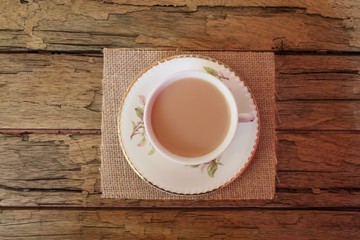 Traditional milky tea served in a bone china cup and saucer on a rough wooden table