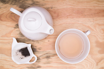 Flat lay - tea cup, tea kettle, small tray and used tea bag on wooden desk