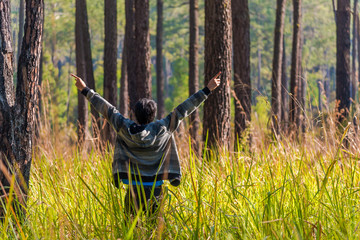Young man spreading hand in green forest around grass.