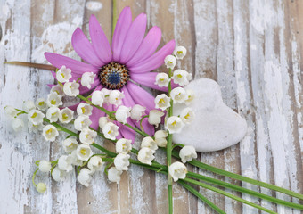 bouquet de muguets et cœur  en pierre sur table bois blanc 