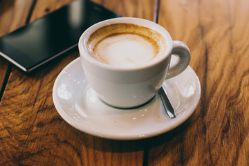 A cup of coffee and smart phone on a wooden table in cafe 