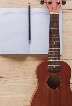 blank notebook with pencil and ukulele on wooden table
