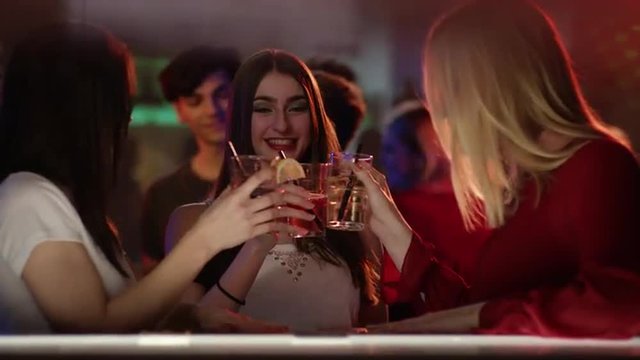 three girls at a bar in a club having a longdrink
