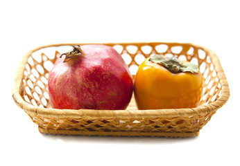 Pomegranate and persimmon in a wicker basket on a white background
