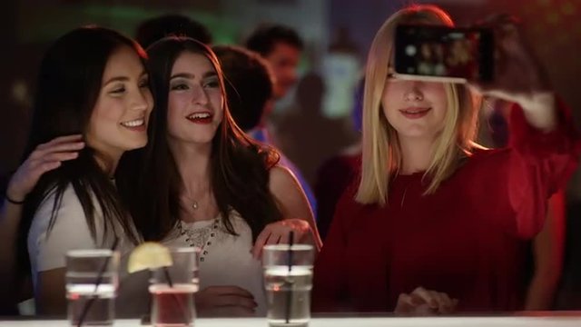 three girls at a bar in a club taking a selfie