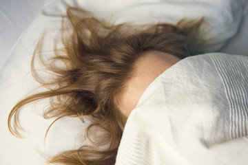 red-haired man lying in bed with bedsheet on face