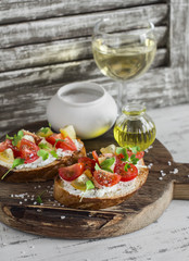 Tomato and cheese bruschetta and glasses of white wine on a rustic wooden cutting board.