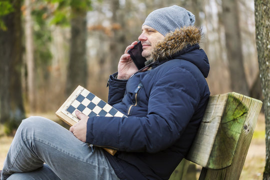 Man with chess talking on smart phone in park