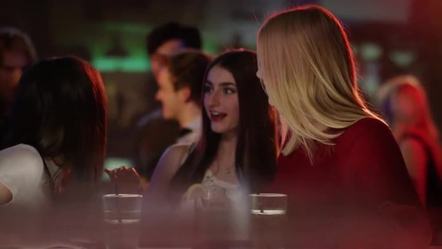 two girls at a bar in a club meet a good friend