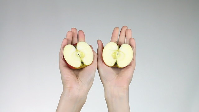 Red apple cut into two parts in female hands.