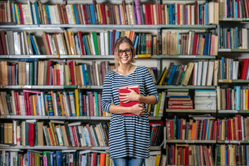 ollege girl holding books in front of a university library book shelf