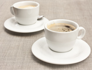 Two cups of coffee on white plates, on burlap texture