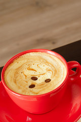 Coffee with cream in a red bowl on a wooden background