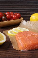 Raw salmon on baking paper, cherry tomatoes, lemon and parsley. Rustic wooden background
