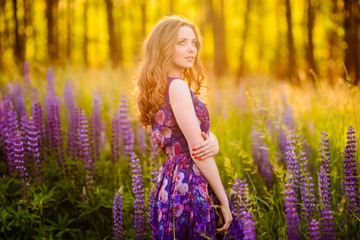 girl with flowers lupines in a field at sunset