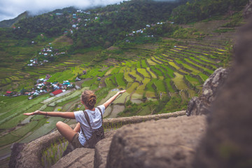 Freedom, travel,success concept.Woman sitting on rice terrace looking at the breathtaking view of rice terraces,cheering the world and spreading out arms.Highest view point.Batad,Ifugao,Philippines.  