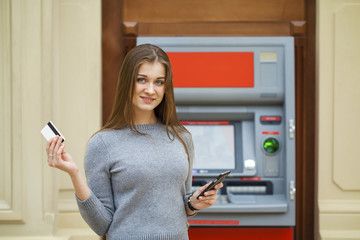 Young happy brunette woman withdrawing money from credit card at