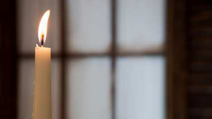 White burning candle on a blurred background of  window