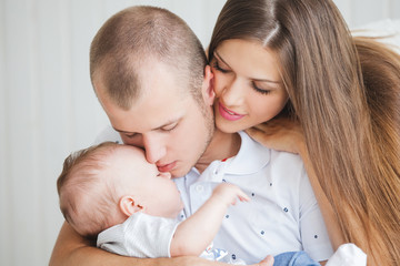 a young family with a nice and sweet little baby sitting on the sofa in a bright interior