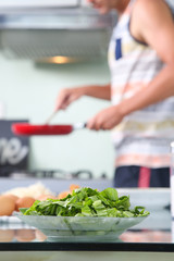 Lunch time! Man holding pan in the kitchen, green veggie in the foreground