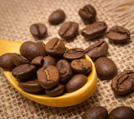 Heap of coffee beans with wooden spoon on jute canvas