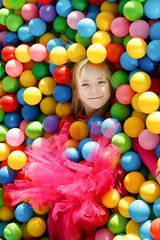 Fototapeta na wymiar Little smiling girl playing lying in colorful balls park playground