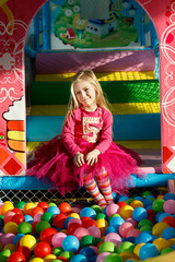 Fototapeta na wymiar Little smiling girl playing lying in colorful balls park playground