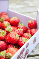 Fresh strawberries in a cardboard carton outside on a wooden table