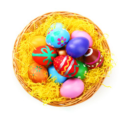 Painted Easter eggs in wicker nest isolated on white