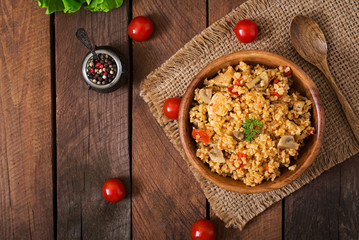 Bulgur with chicken, mushrooms and tomatoes in a wooden bowl. Top view