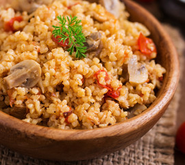 Bulgur with chicken, mushrooms and tomatoes in a wooden bowl. Top view