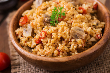 Bulgur with chicken, mushrooms and tomatoes in a wooden bowl. Top view
