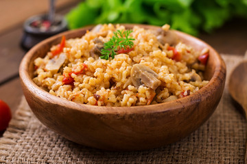 Bulgur with chicken, mushrooms and tomatoes in a wooden bowl. Top view