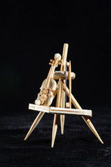 Wooden miniature of violin and stick on black background. Violin standing on wooden stand. Macro shot.