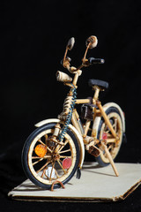 Obraz premium Miniature handicraft of wooden bicycle on black background standing on wooden stand. Macro shot.