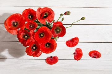 Bouquet of red poppies in glass vase and poppy petals near on ol