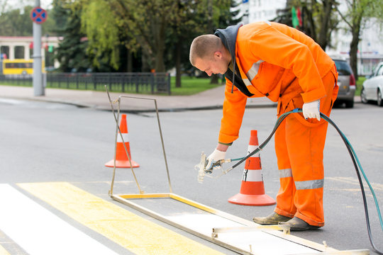 Road painter man worker marking street lines zebra crossing traffic sign using paint sprayer gun