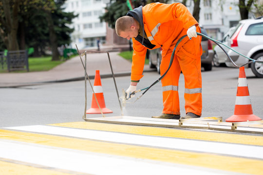 Road worker marking zebra crossing traffic sign using paint sprayer gun