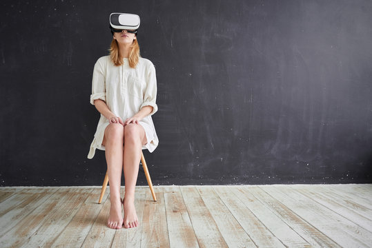 The girl in white sitting on a chair in the virtual reality helmet