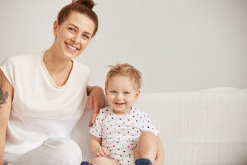 Young mother with her one years old little son dressed in pajamas are relaxing and playing in the bed at the weekend together, lazy morning, warm and cozy scene. Selective focus