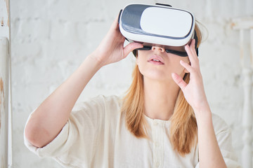 The girl in white standing against a white wall in a virtual reality helmet