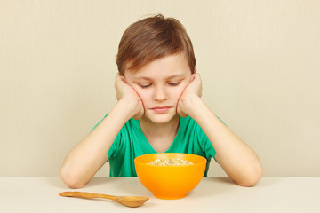 Little displeased boy does not want to eat a porridge